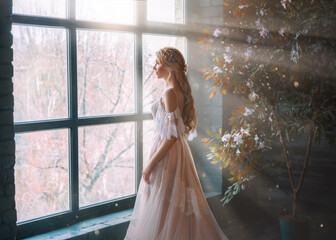 Romantic lady, blonde woman with long hair in white vintage dress stands in dark room, looks out...