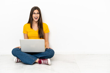 Young woman with a laptop sitting on the floor with surprise facial expression