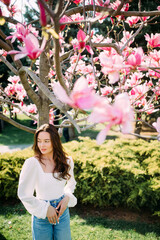 Woman stands in garden under the blooming magnolia tree.