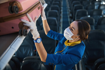 Airline stewardess carefully putting pink suitcase into luggage rack