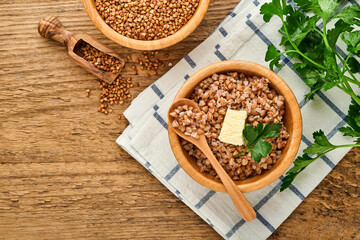 Buckwheat porridge in bowl with parsley leaf and butter on old wooden background. Gluten free ancient grain for healthy diet. Top view. Copy space.