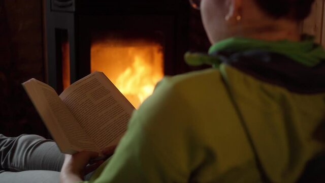 Young woman reading a book near fireplace at home.