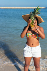 Woman with a pineapple on her face walks on the beach