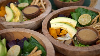 Raw and rustic plant based lunch. Vegetables, leaves and avocado served in wooden bowls. 