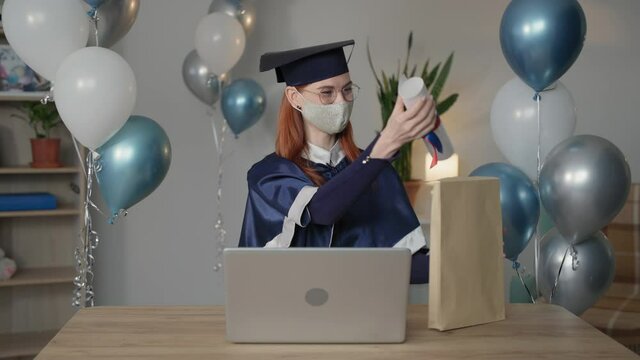 quarantine graduation, cute student of university in academic mantle rejoices diploma online sitting at home during virtual graduation ceremony during distance education