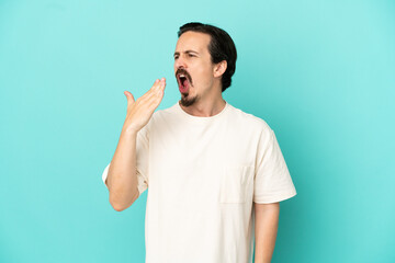Fototapeta premium Young caucasian man isolated on blue background yawning and covering wide open mouth with hand