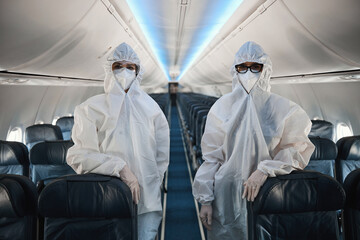 Two cabin crew workers in protective overalls in plane cabin