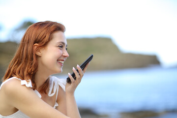 Happy woman using voice recognition on phone on the beach
