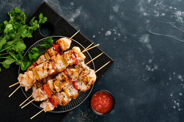 Chicken shish kebab or skewers kebab on wooden board, spices, herbs and vegetables on dark grey background. Barbecue Raw ingredients for goulash or shish kebab. Top view. Free copy space.