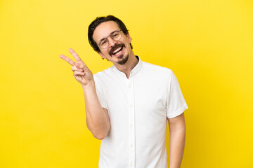 Young caucasian man isolated on yellow background smiling and showing victory sign