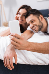 Blurred couple taking selfie on smartphone on bed