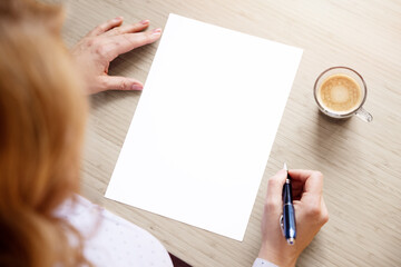 Woman sitting at desk with pen in hand and looking at blank white sheet of paper