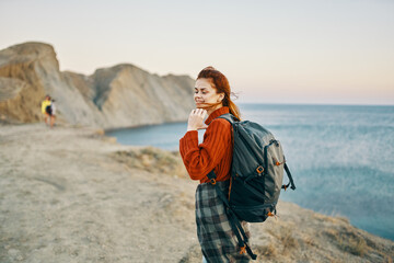 a traveler in the mountains with a backpack on her back goes to the side and the sea is nearby