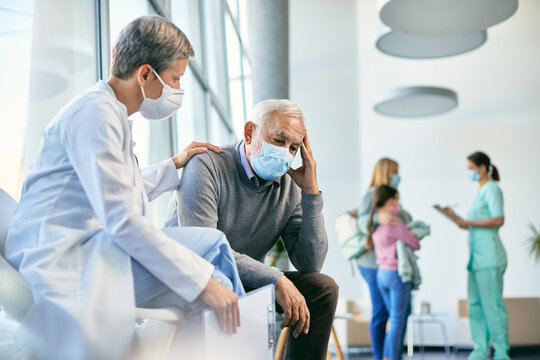 Worried senior man being consoled by female doctor in waiting room at the hospital during COVID-19 pandemic.