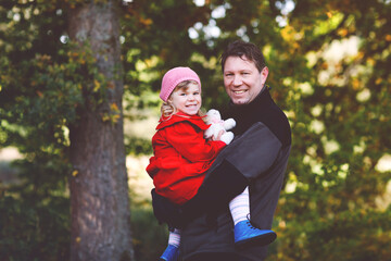 Happy young father having fun cute toddler daughter, family portrait together. Middle-aged Man with beautiful baby girl in autumn forest or park. Dad with little child outdoors, hugging. Love, bonding