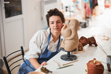 Woman ceramist posing for camera near clay model
