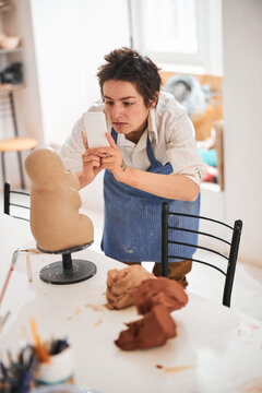 Pottery craftswoman bending for taking a photo of figure