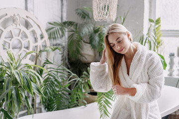 Young woman in bathrobe touching hair, standing in bathroom