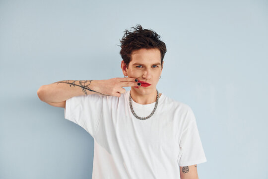 Young gay man is standing in the studio and posing for a camera. Lips in red lipstick