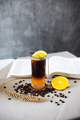 Orange black coffee and open book on the coffee table surrounded with coffee bean.