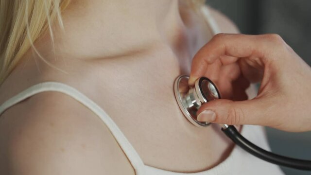 The doctor listens to the patient with a stethoscope close-up. Doctor's hand listens with a stethoscope to a young woman. At the doctor's appointment. 4K UHD