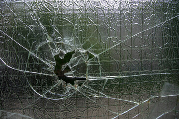Crack from impact on corrugated glass with a greenish tint and frosty pattern