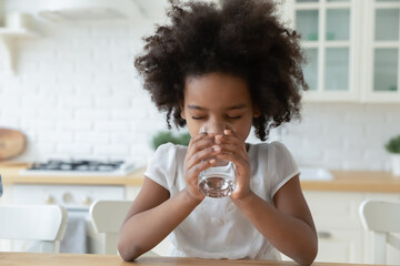 Thirsty little African American kid feel dehydrated enjoy clean mineral water from glass. Small...