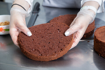 Womans hands chef holding chocolate cake layers and stacking them on metal table