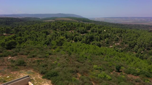 Aerial Shot Of Tourists Exploring Structure By Israeli Flag, Drone Flying Forward Over Green Forest On Sunny Day - Megiddo, Israel