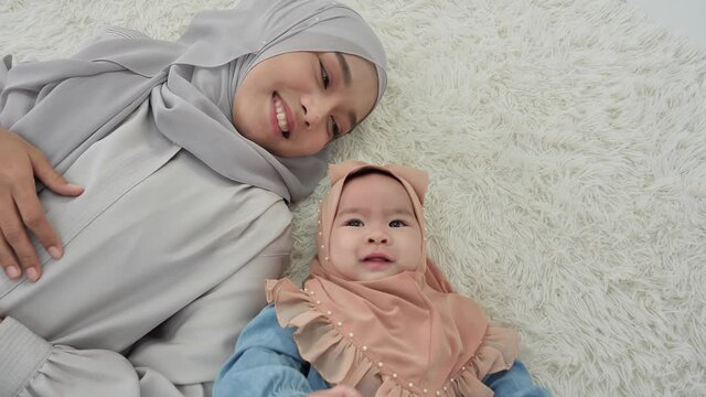 Top view Mother and baby girl 6 months old in traditional hijab clothing Lying Down on floor in bedroom. slow motion