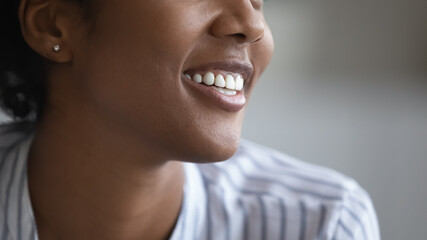 Close up happy millennial generation african multiracial woman with healthy toothy white smile looking in distance, feeling satisfied with professional orthodontic service, dental clinic concept.