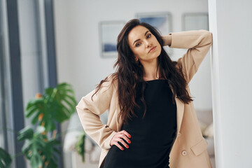 Fototapeta premium In black dress and jacket. European woman in fashionable stylish clothes is posing indoors