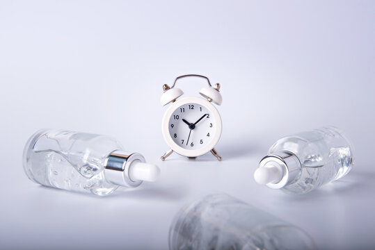 Bottles of face serum are lying around on a white table around the clock.