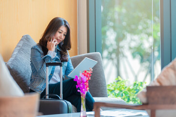 Asian woman with suitcase using mobile phone for calling and using application on tablet for contact customer service and order cab taxi after arrival to airport terminal. Copy Space