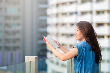 Asia woman reading book at outdoor balcony and blur background many building in urban. Copy spaceBeautiful young asian woman reading book at outdoor balcony and blur background many building in urban.