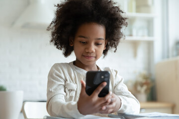 Fototapeta na wymiar Happy smart little African American girl kid hold modern cellphone gadget talk on video call online. Small 8s biracial child use smartphone have webcam virtual event. Children technology concept.