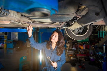 Car service, Advertising, Business Concept - Asian woman mechanic holding wrench and checking the car suspension. Vehicle raised on lift at maintenance station. Copy space, Selective Focus