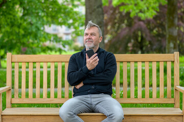 Obraz premium Middle-aged man relaxing on a park bench with his mobile