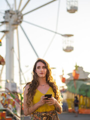 Mujer joven usando su teléfono móvil en un parque de atracciones o en una feria 