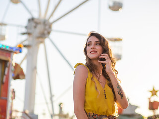 Mujer joven hablando por teléfono en una feria o parque de atracciones 