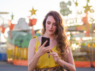 Mujer joven usando su teléfono móvil en un parque de atracciones o en una feria 