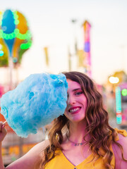 Mujer joven disfrutando de un algodón de azúcar en la feria o parque de atracciones