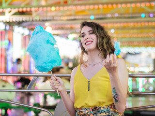 Mujer joven disfrutando de un algodón de azúcar en la feria o parque de atracciones