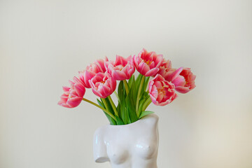 Conceptual image of bi-color tulips bouquet in ceramic venus de milo shaped vase over white wall background with a lot of copy space for text. Close up.