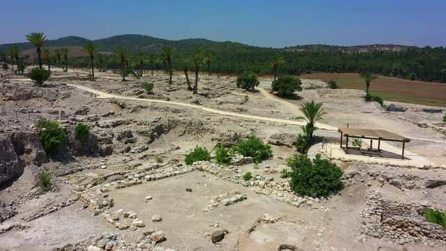 Aerial Panning Shot Of Palm Trees At Tel Megiddo Near Houses, Drone Flying Forward Over Protected Site On Sunny Day