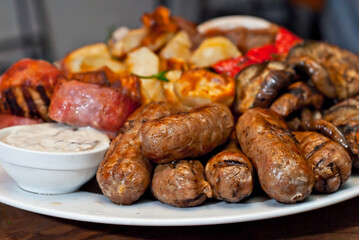 Assorted meat on a plate close up. Different types of meat and potatoes in a heap. Appetizer on a large plate with sauces.