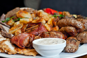 Assorted meat on a plate close up. Different types of meat and potatoes in a heap. Appetizer on a large plate with sauces.