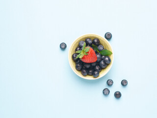 Bowl of fresh blueberries and a strawberry on a blue background