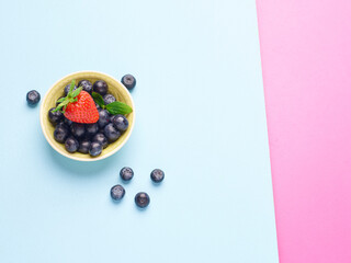 Bowl of fresh blueberries and a strawberry on a blue and pink background