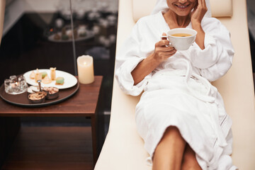 Charming beautiful elegant woman in white bathrobe drinking beverage while spending time in spa resort hotel